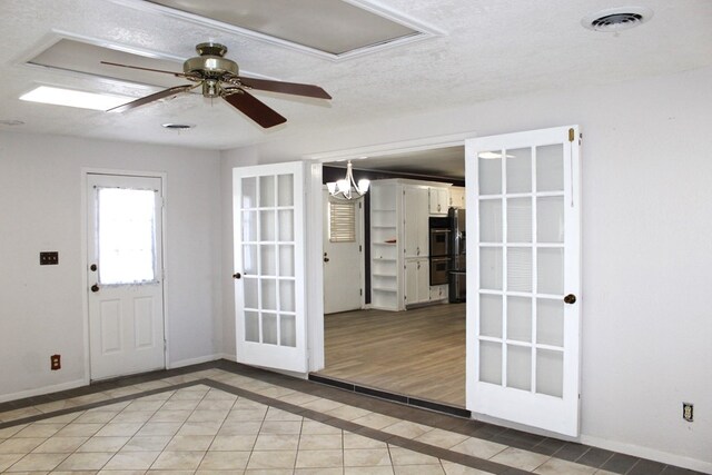 doorway with french doors, ceiling fan with notable chandelier, light hardwood / wood-style floors, and a textured ceiling