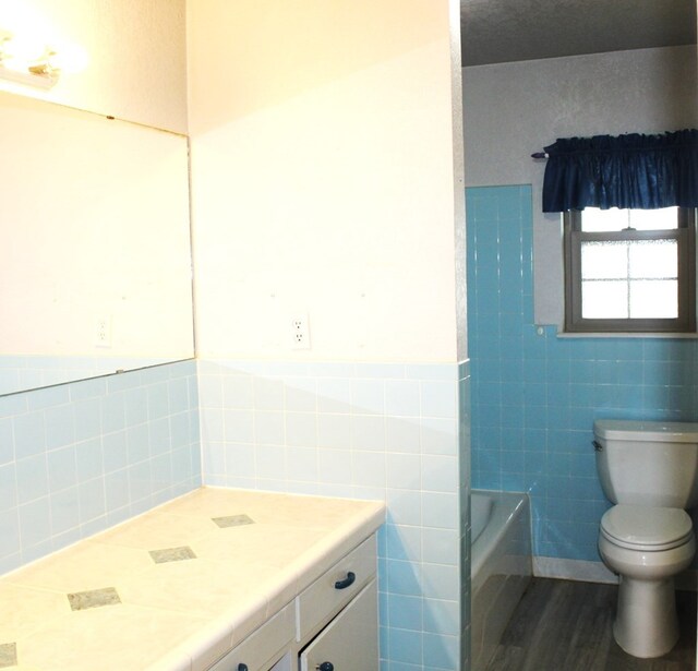 bathroom featuring hardwood / wood-style floors, vanity, a bathtub, toilet, and tile walls