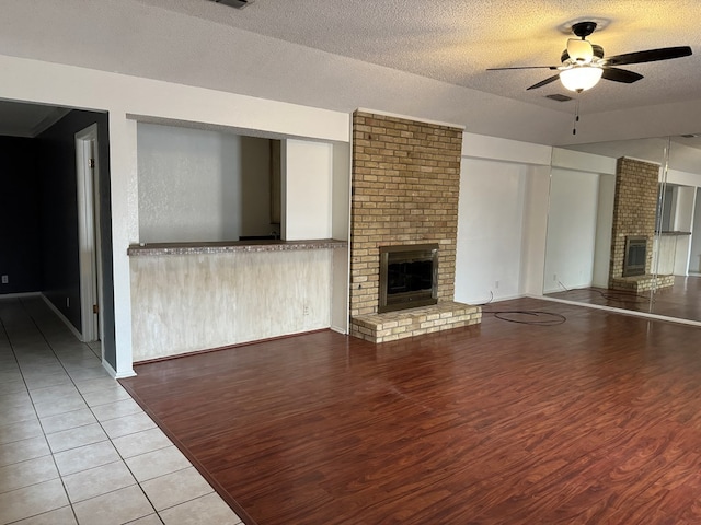 unfurnished living room with ceiling fan, light wood-type flooring, a textured ceiling, and a fireplace