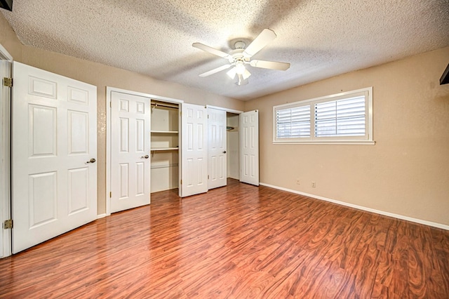 unfurnished bedroom with hardwood / wood-style flooring, ceiling fan, multiple closets, and a textured ceiling