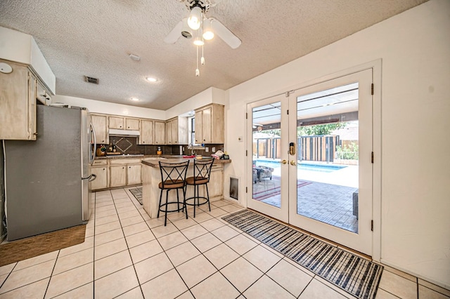 kitchen with light tile patterned flooring, stainless steel refrigerator, light brown cabinetry, a kitchen bar, and french doors