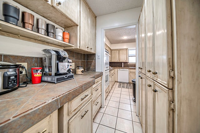 kitchen with tile countertops, a textured ceiling, light tile patterned floors, white appliances, and decorative backsplash