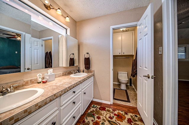 bathroom with toilet, a textured ceiling, vanity, hardwood / wood-style flooring, and ceiling fan