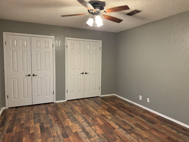 unfurnished bedroom featuring multiple closets, ceiling fan, a textured ceiling, and dark hardwood / wood-style flooring