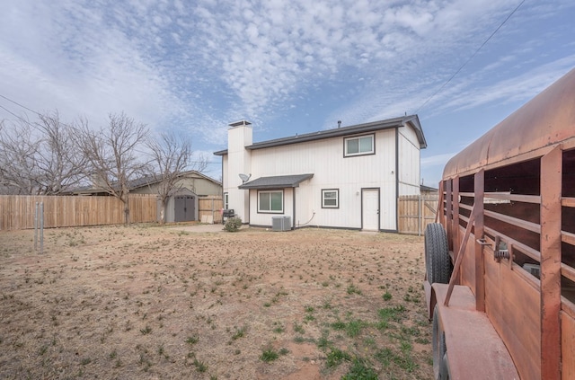 rear view of property with a chimney, central AC unit, and an outbuilding