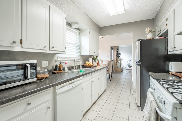 kitchen featuring light tile patterned flooring, white appliances, a sink, white cabinetry, and dark countertops