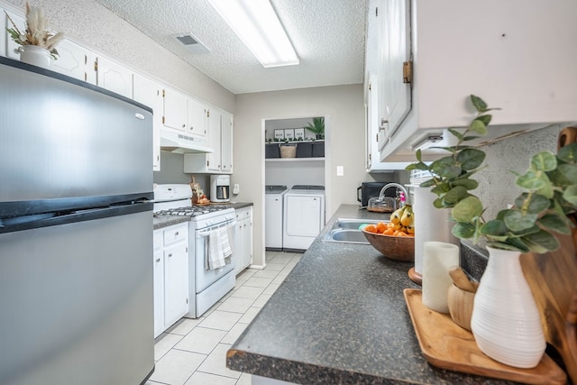 kitchen with white gas range, freestanding refrigerator, washing machine and dryer, a sink, and under cabinet range hood