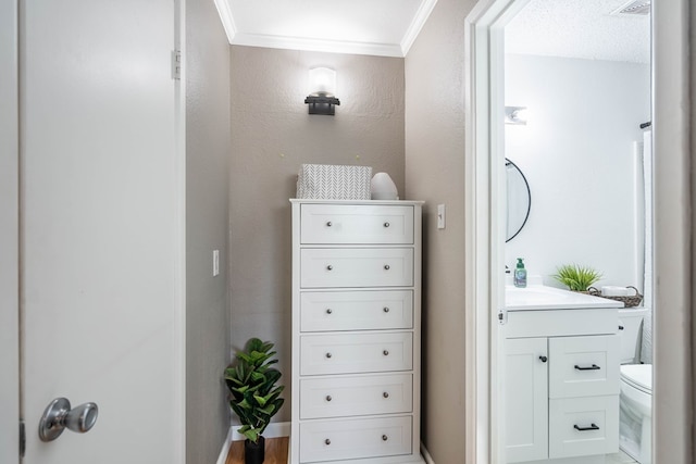 half bathroom with crown molding, visible vents, a textured wall, toilet, and vanity