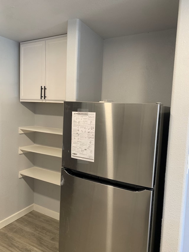 interior details featuring stainless steel fridge, white cabinets, and dark hardwood / wood-style floors