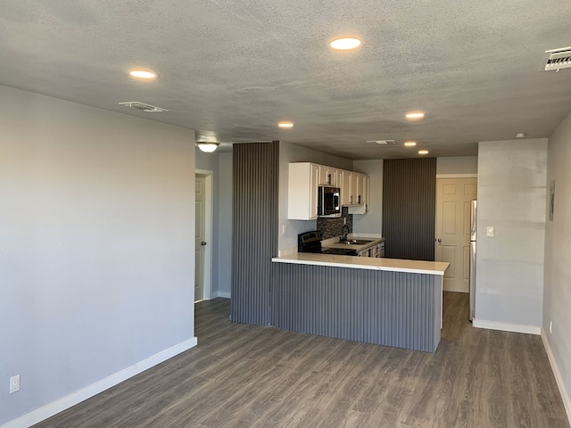 kitchen with kitchen peninsula, appliances with stainless steel finishes, a kitchen bar, dark hardwood / wood-style flooring, and white cabinetry