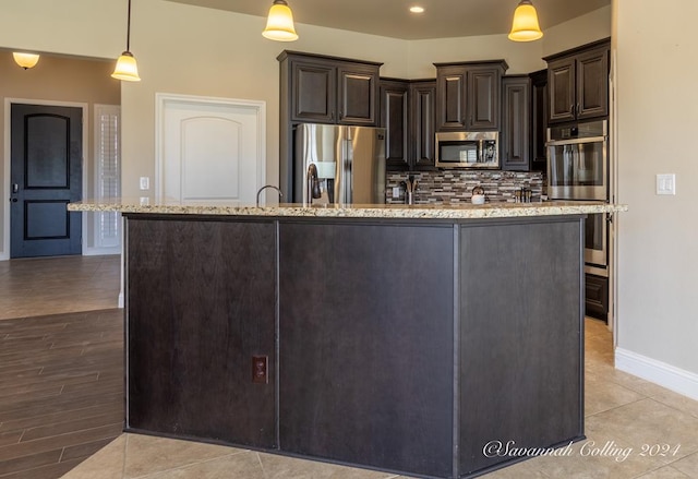 kitchen featuring pendant lighting, an island with sink, stainless steel appliances, and dark brown cabinets