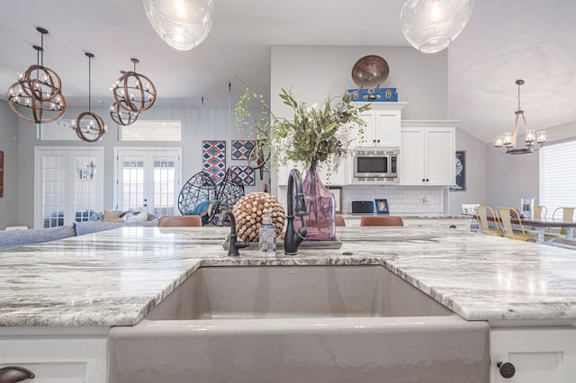 kitchen with sink, white cabinetry, stainless steel microwave, french doors, and a chandelier