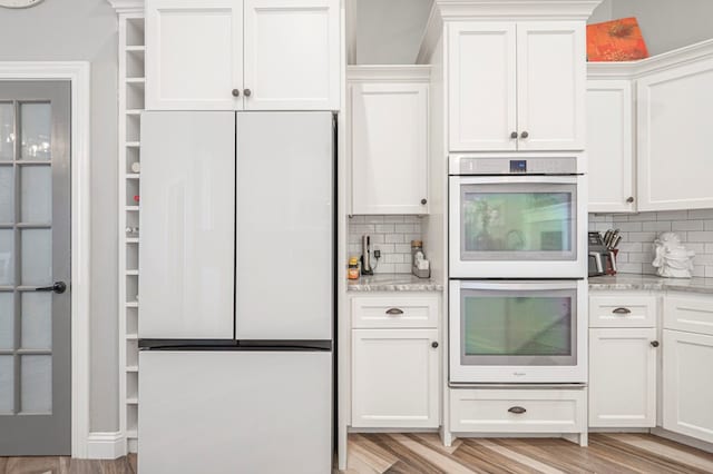 kitchen featuring fridge, white cabinetry, double oven, and light stone counters