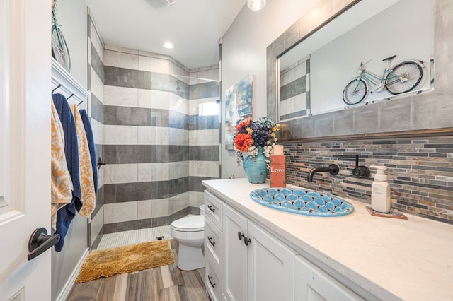 bathroom featuring backsplash, a tile shower, vanity, wood-type flooring, and toilet