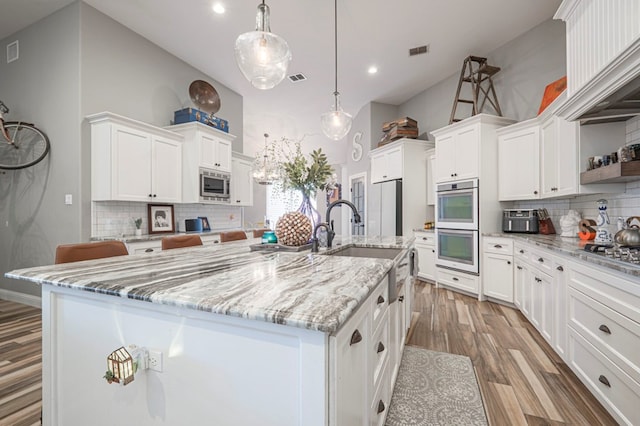 kitchen with an island with sink, stainless steel microwave, white cabinets, and decorative light fixtures