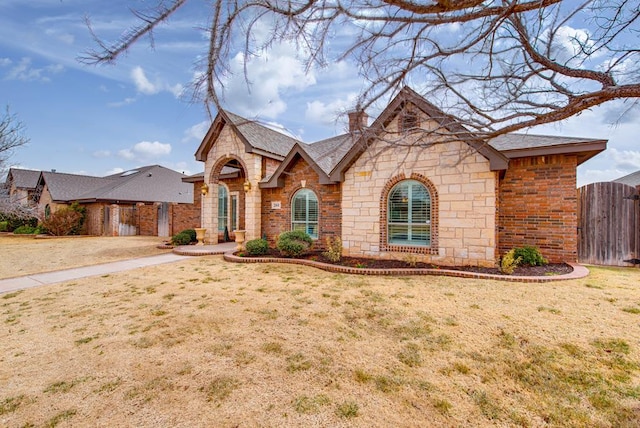 view of front facade featuring brick siding, stone siding, a gate, a front lawn, and a chimney