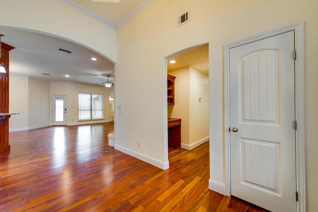 empty room featuring arched walkways, crown molding, visible vents, ceiling fan, and wood finished floors