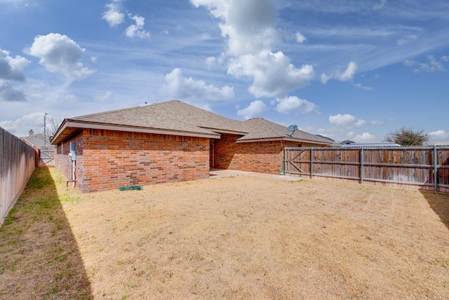 back of property featuring a shingled roof, brick siding, and a fenced backyard