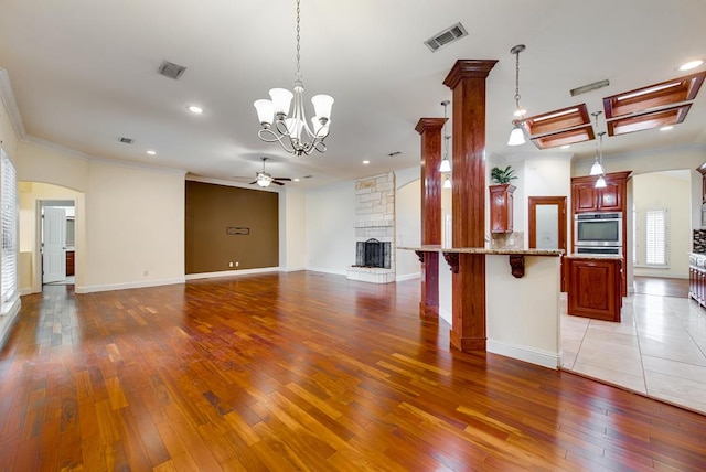 kitchen featuring hanging light fixtures, ceiling fan with notable chandelier, visible vents, and a stone fireplace