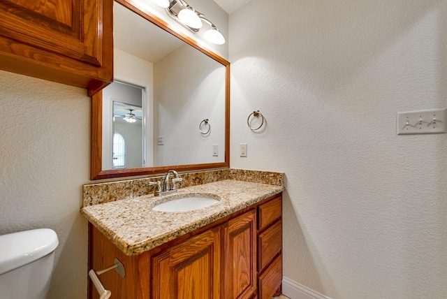 bathroom with toilet, a textured wall, and vanity