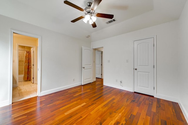 unfurnished bedroom with wood-type flooring, connected bathroom, visible vents, and baseboards