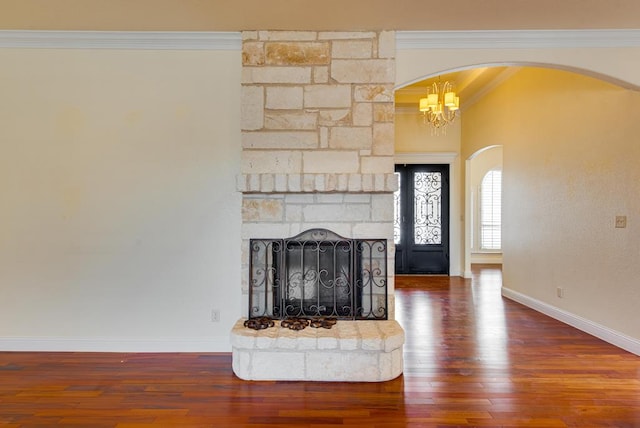 unfurnished living room with arched walkways, crown molding, a stone fireplace, wood finished floors, and baseboards