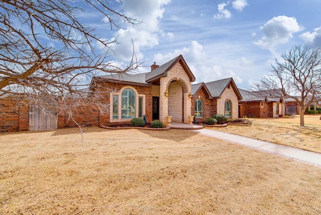 view of front of house featuring a shingled roof, stone siding, a chimney, and a front lawn