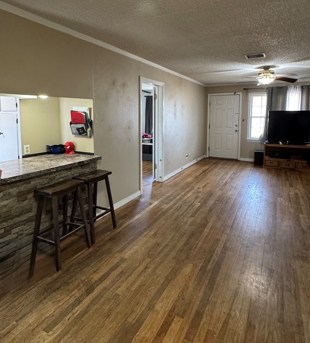 unfurnished living room with dark wood-type flooring, ceiling fan, crown molding, and a textured ceiling