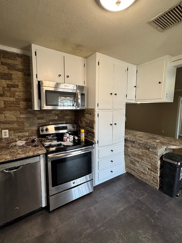 kitchen with a textured ceiling, appliances with stainless steel finishes, dark stone counters, decorative backsplash, and white cabinets