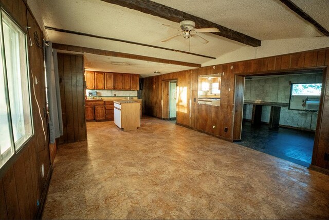 kitchen featuring a textured ceiling, ceiling fan, wooden walls, lofted ceiling with beams, and a kitchen island