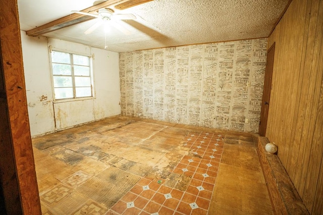 empty room featuring wood walls, ceiling fan, and a textured ceiling