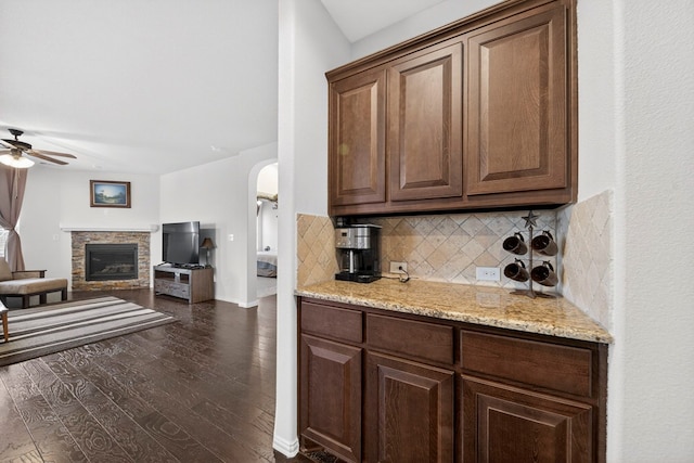 5001 Shadybrook Rd, Midland, TX 79705 - kitchen featuring a ceiling fan, decorative backsplash, dark wood-style flooring, arched walkways, and light stone counters