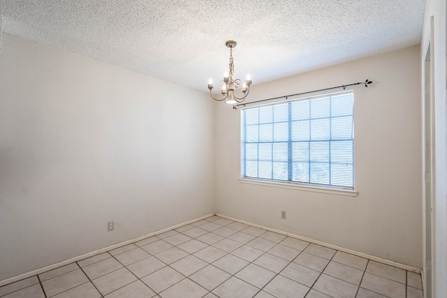 empty room featuring a textured ceiling, light tile patterned flooring, and a notable chandelier