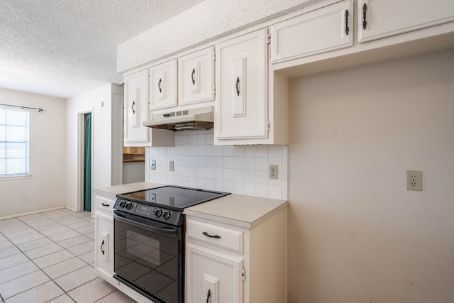 kitchen with light tile patterned floors, black / electric stove, under cabinet range hood, light countertops, and backsplash