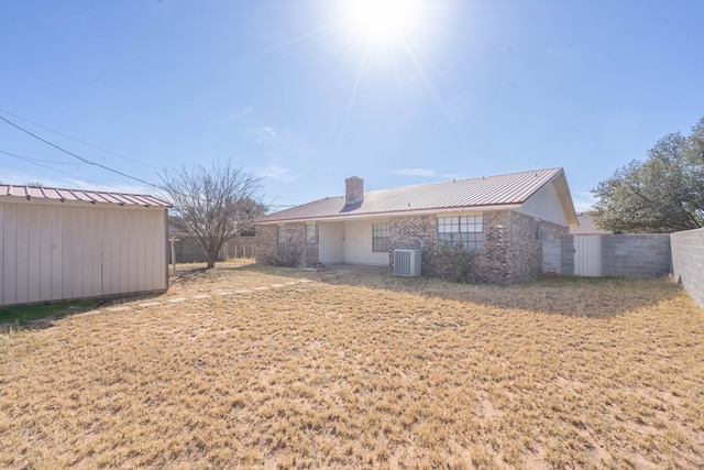 rear view of house with a chimney, metal roof, an outbuilding, fence, and cooling unit