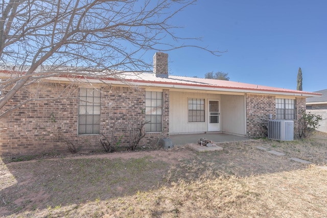 rear view of house featuring a chimney, metal roof, central AC, and brick siding