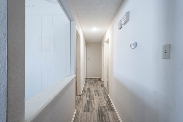 corridor with a textured ceiling, wood finished floors, and baseboards