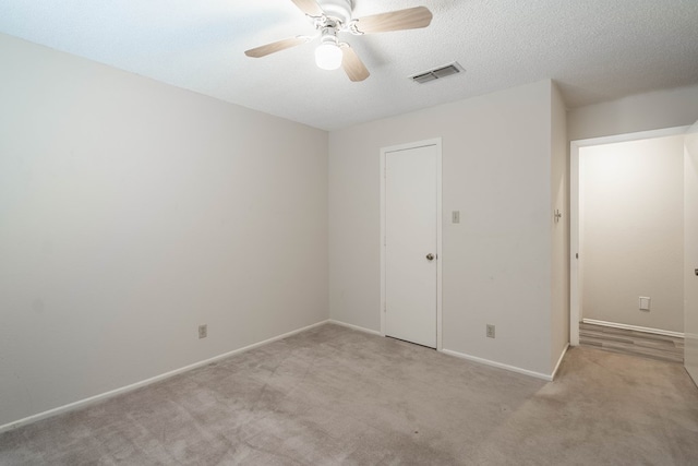 empty room with baseboards, visible vents, a ceiling fan, a textured ceiling, and carpet flooring