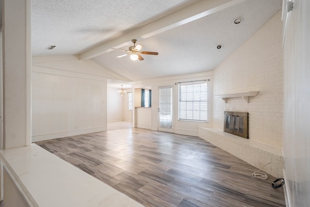 unfurnished living room featuring vaulted ceiling with beams, a textured ceiling, ceiling fan with notable chandelier, a fireplace, and wood finished floors