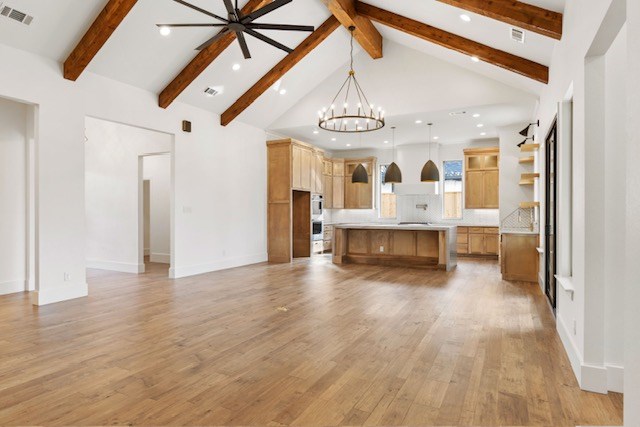 unfurnished living room featuring beamed ceiling, high vaulted ceiling, ceiling fan with notable chandelier, and light wood-type flooring