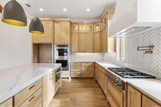 kitchen featuring light stone countertops, wall chimney exhaust hood, stainless steel appliances, decorative light fixtures, and light hardwood / wood-style flooring