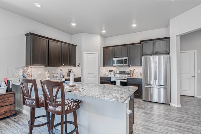 1407 Derrick Ave, Odessa, TX 79765 - kitchen with stainless steel appliances, dark brown cabinets, light wood-style floors, a breakfast bar area, and recessed lighting