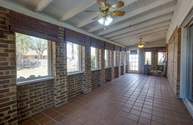 unfurnished sunroom featuring ceiling fan, beam ceiling, and brick wall