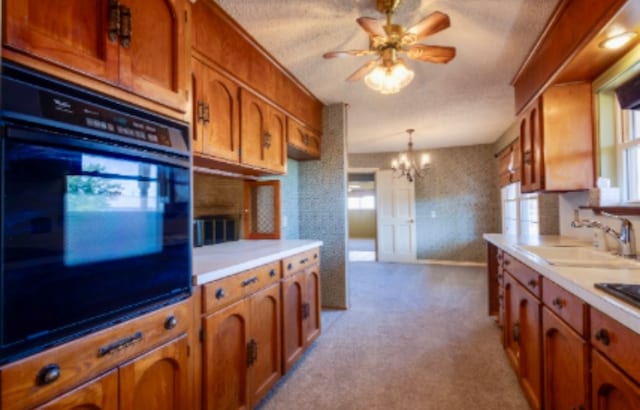 kitchen featuring brown cabinetry, a sink, light countertops, ceiling fan with notable chandelier, and carpet