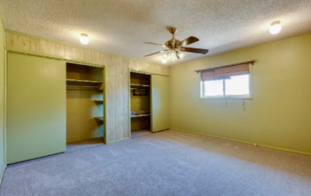 unfurnished bedroom featuring baseboards, two closets, a textured ceiling, and light colored carpet