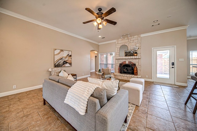 living room with ceiling fan, a stone fireplace, crown molding, and plenty of natural light