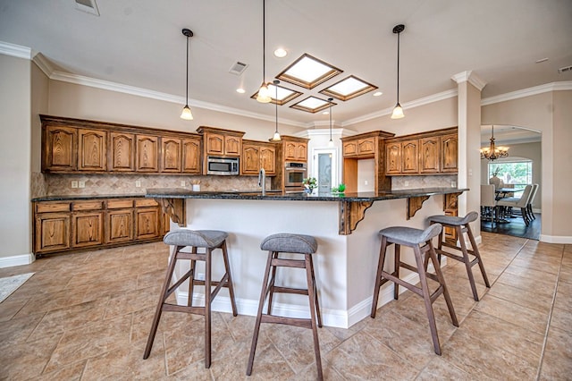 kitchen featuring hanging light fixtures, stainless steel appliances, a center island with sink, backsplash, and a breakfast bar area