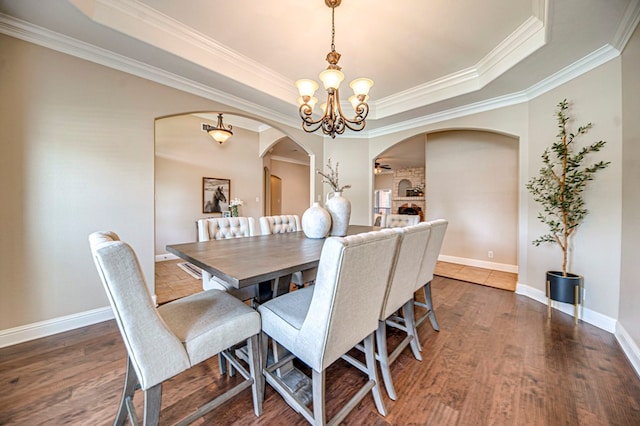 dining space with dark hardwood / wood-style flooring, a raised ceiling, ornamental molding, and a stone fireplace