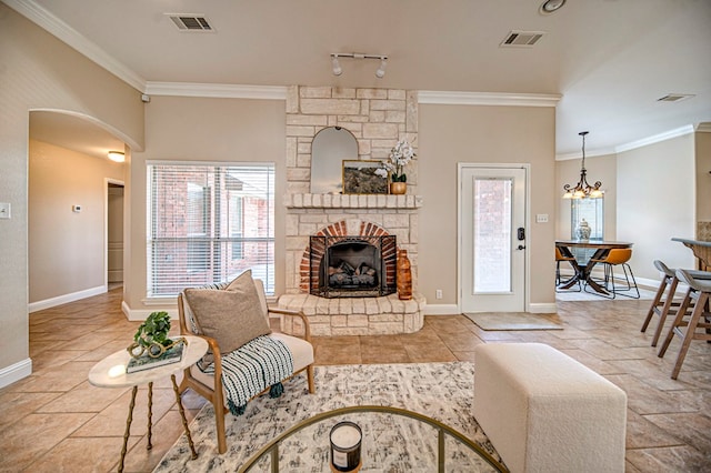 living room with ornamental molding, a stone fireplace, an inviting chandelier, and rail lighting