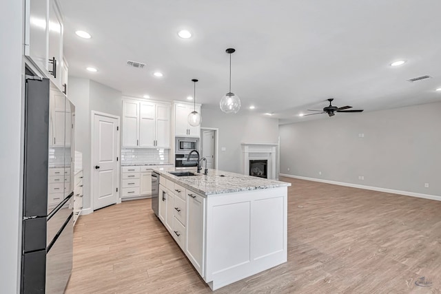 kitchen featuring sink, white cabinetry, hanging light fixtures, appliances with stainless steel finishes, and a kitchen island with sink